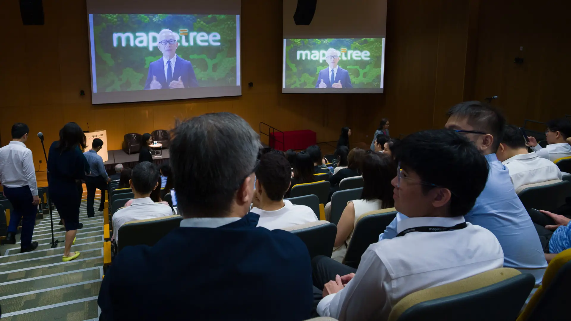 Audience watching a Mapletree corporate townhall video presentation in an auditorium with dual projection screens and on-site AV support.